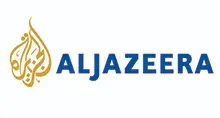 - The official logo for Al Jazeera. It features the brand's iconic gold Arabic calligraphy emblem on the left, followed by the name "ALJAZEERA" in bold, blue sans-serif capital letters. The entire logo is set against a solid white background.